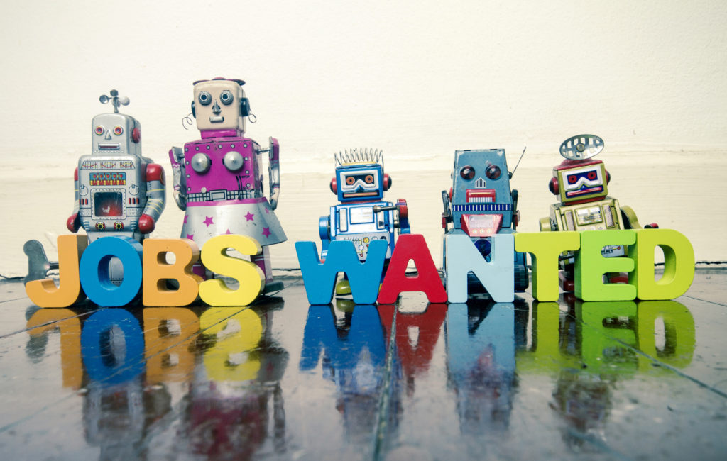 the words JOBS WANTED with wooden letters and robot toys on a wooden floor with reflection